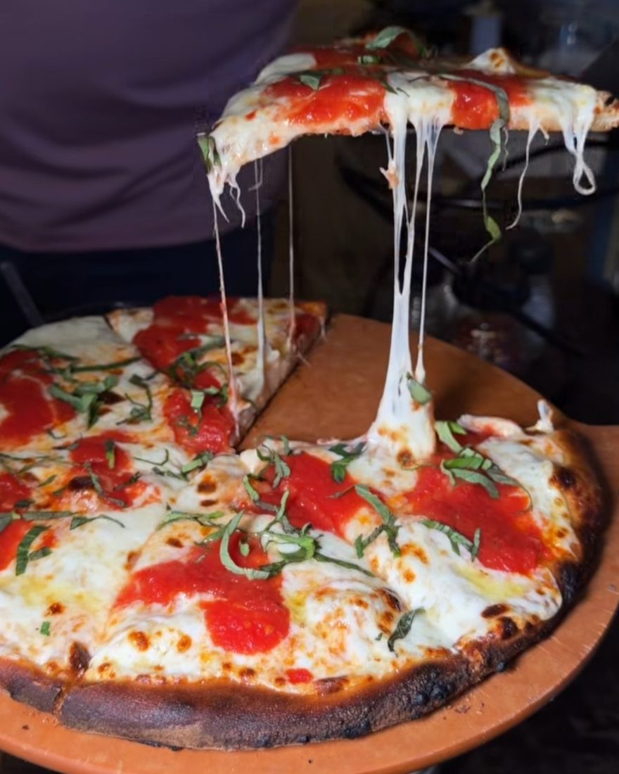 A slice lifted from a wood-fired Margherita pizza, mozzarella stretching