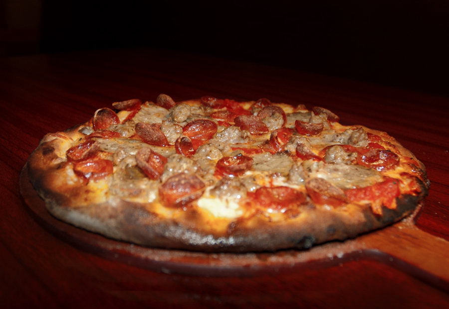 Wood-fired sausage pizza on a serving board