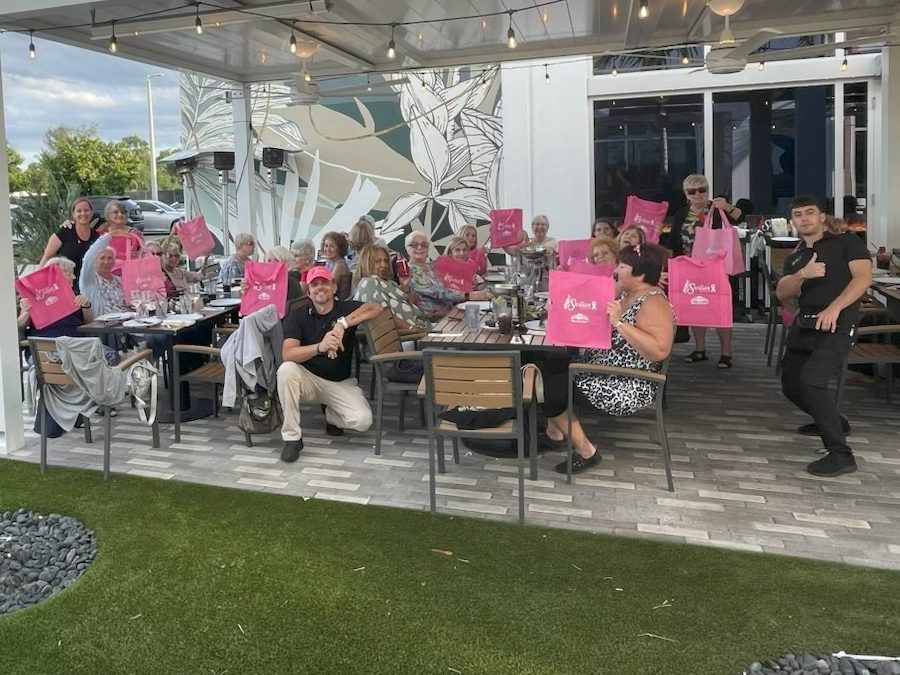 Guests on a Sicilian Oven patio holding up pink Think Pink tote bags